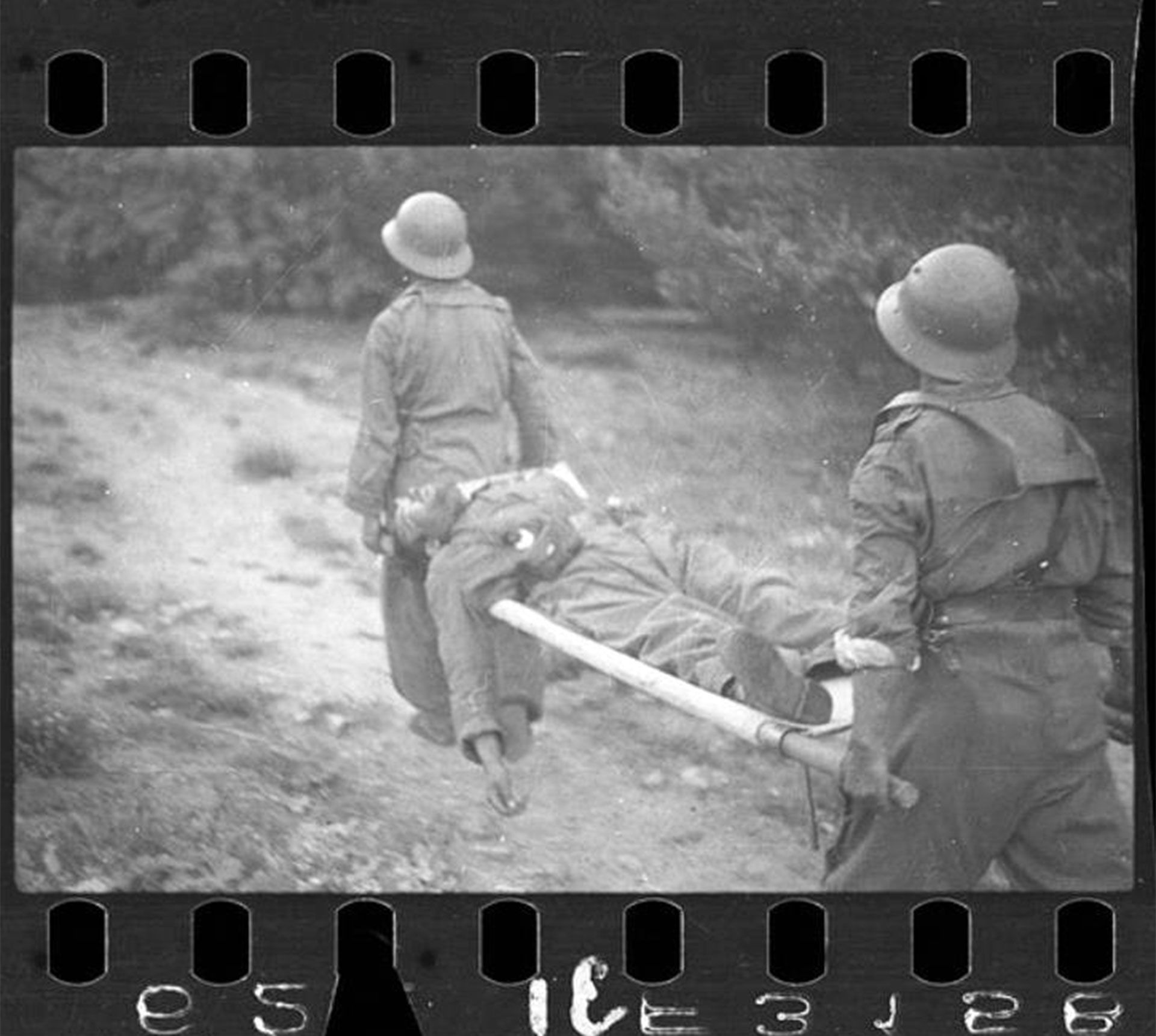 “Dos soldados republicanos con un soldado en una camilla” es el nombre de la fotografía tomada por Taro en Puerto de Navacerrada, frente de Segovia, España, a finales de mayo-principios de junio de 1937. Se trata de uno de los negativos recuperados con material de la fotoperiodista