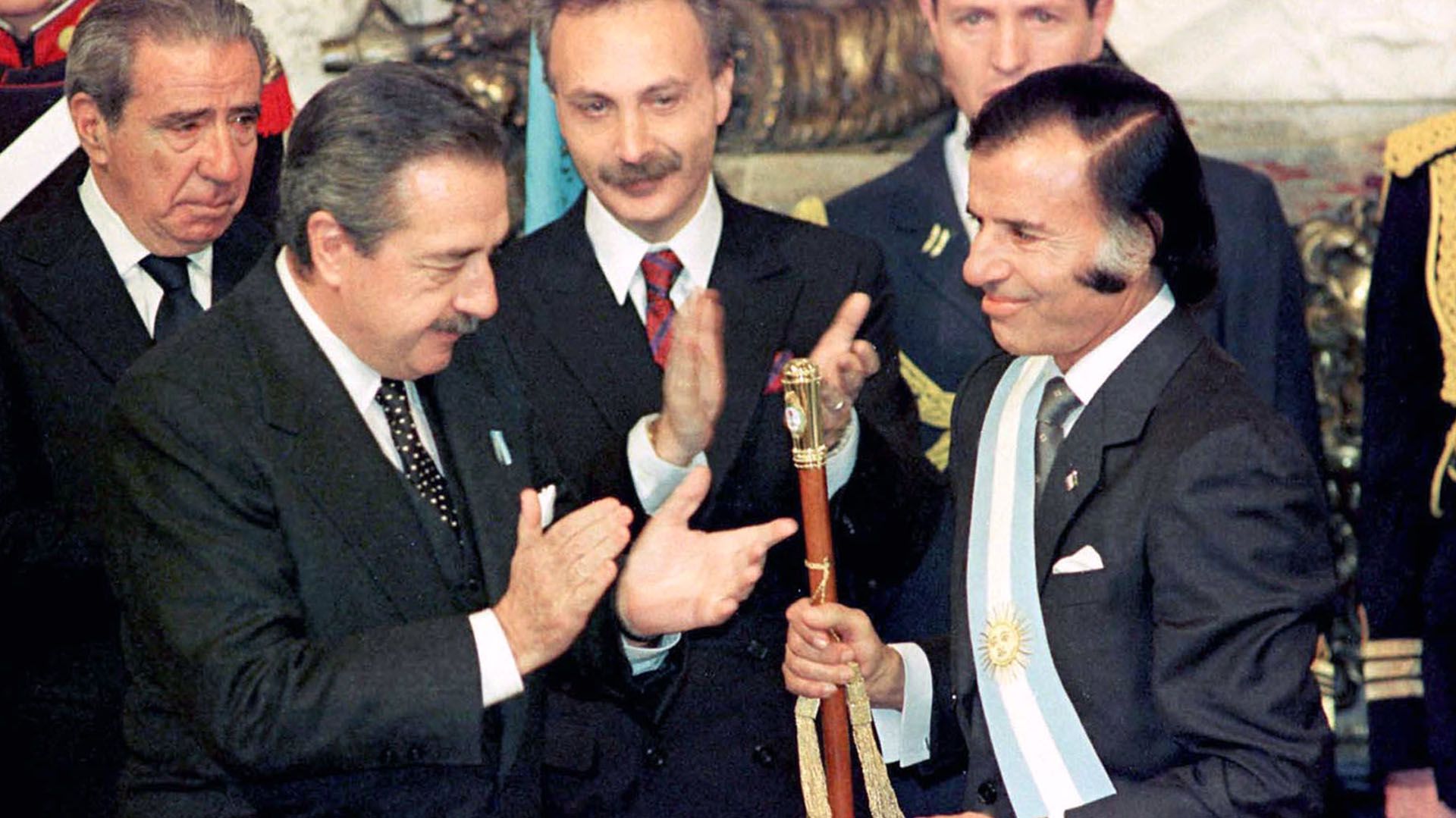 Raúl Alfonsín entrega la banda y el bastón presidencial a Carlos Menem, que llegó antes al gobierno por la crisis institucional que demolió a la administración radical