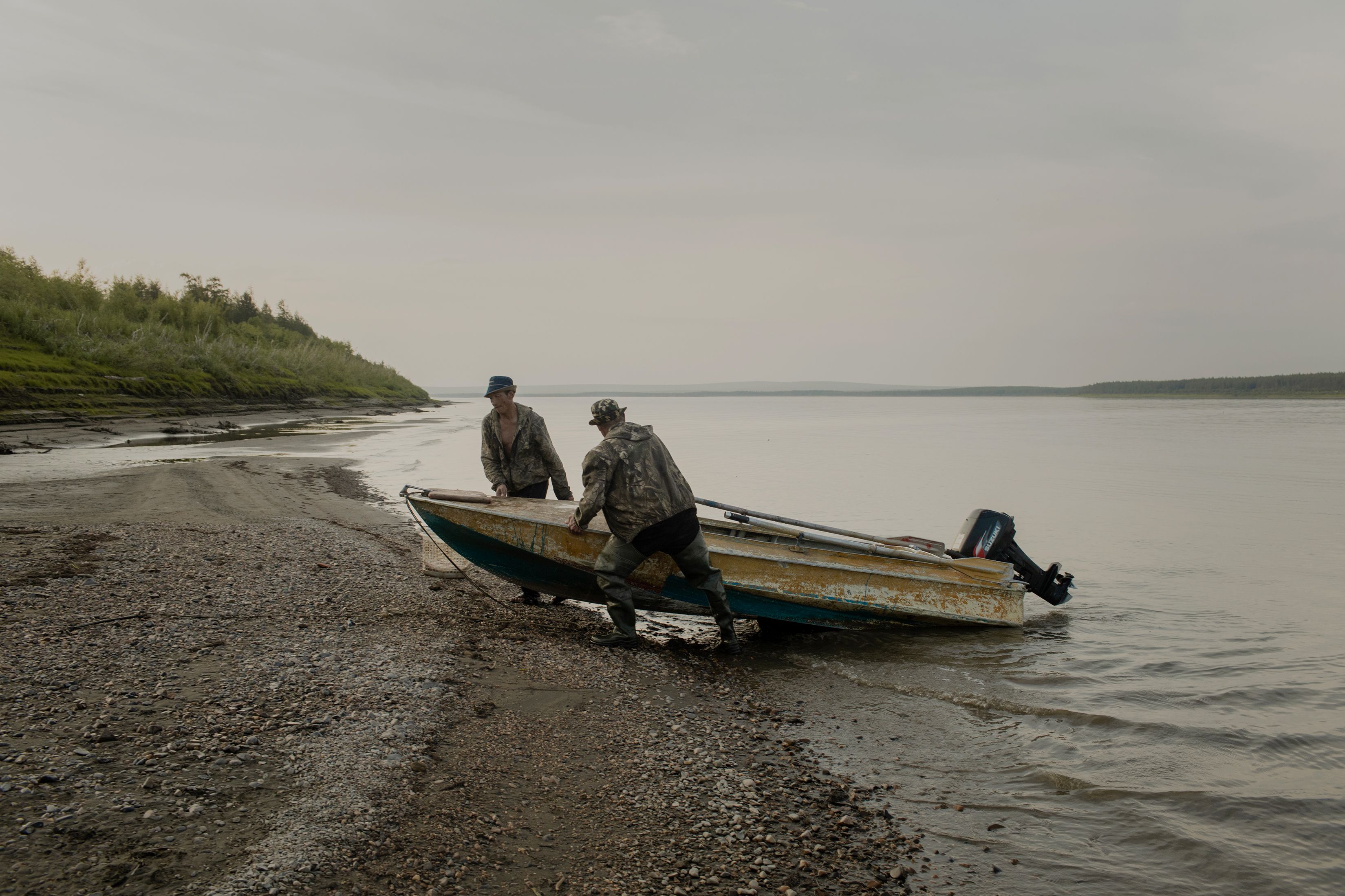 Pescadores sacando un bote del río Kolimá, al noreste de Sajá, cerca de las nueve de la noche. En el verano, el sol nunca se oculta por completo en esa región. (Emile Ducke/The New York Times)