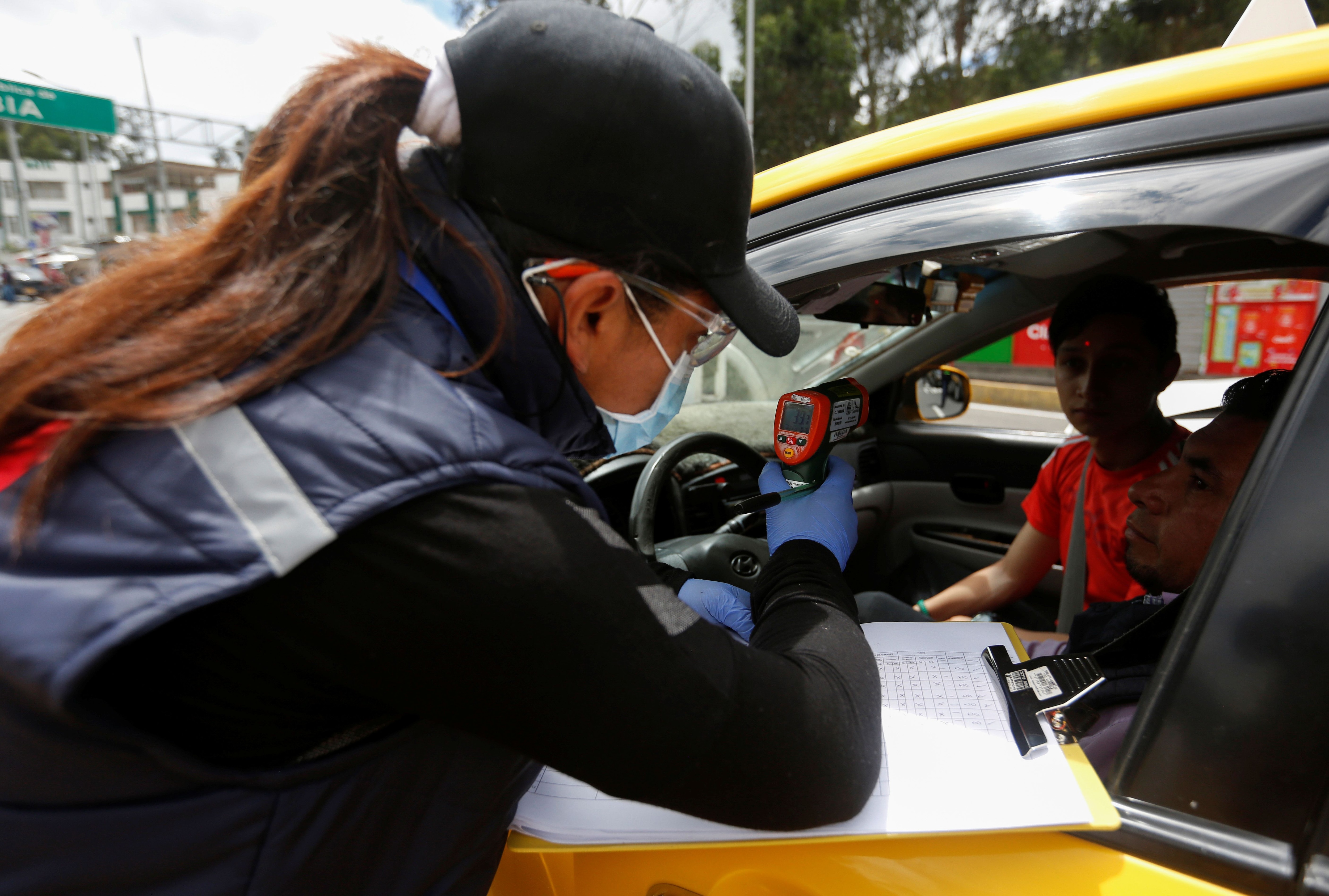 Un oficial de salud colombiano usa una máscara facial protectora mientras revisa a un niño con un escáner térmico mientras cruza la frontera entre Colombia y Ecuador. REUTERS/Daniel Tapia