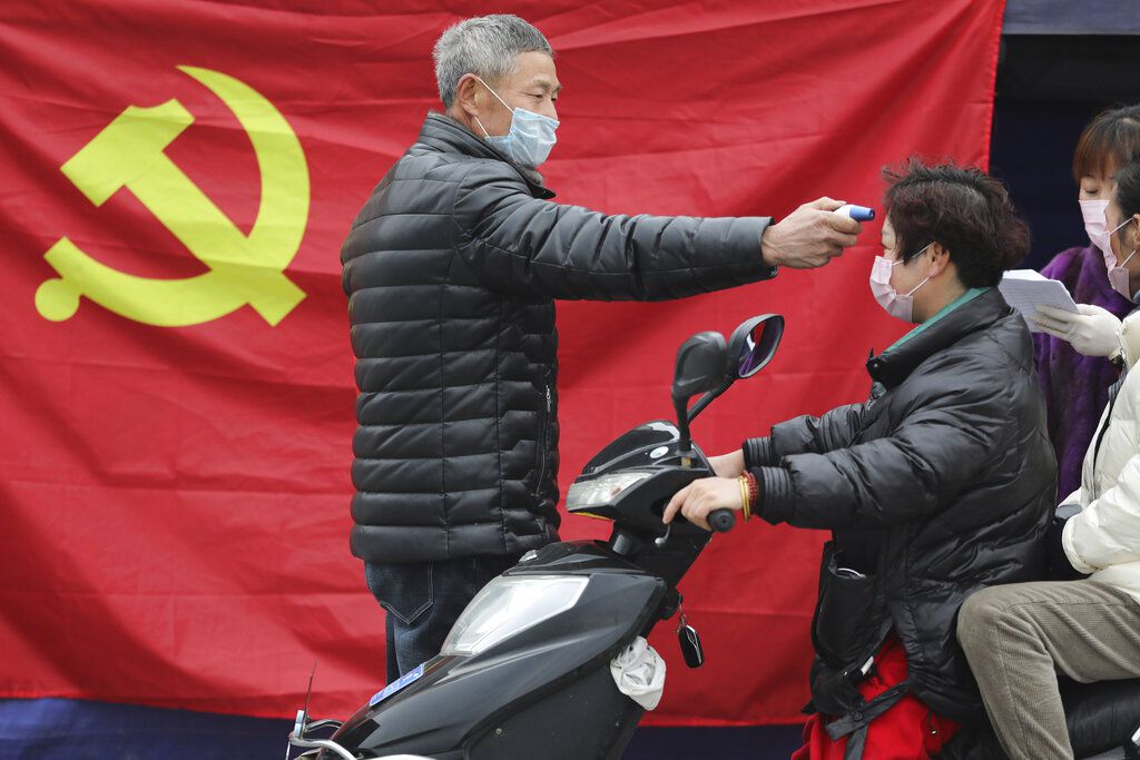 Un voluntario frente a una bandera del Partido Comunista le toma la temperatura a una persona que conduce una moto en un retén en Hangzhou, en la provincia oriental de Zhejiang (Chinatopix vía AP/archivo)