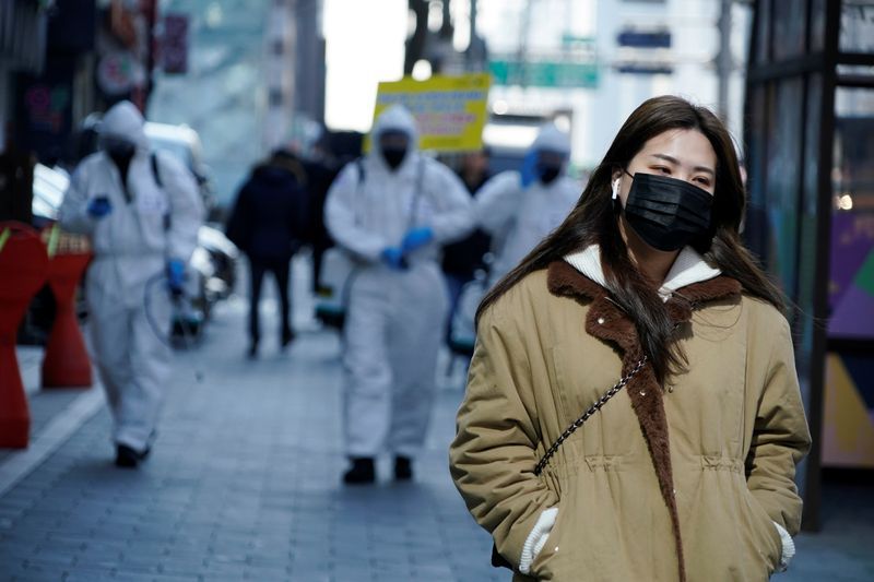 Una mujer ataviada con una mascarilla protectora pasa junto a unos soldados surcoreanos vestidos con equipo sanitario en una calle de Seúl (REUTERS/Kim Hong-Ji)