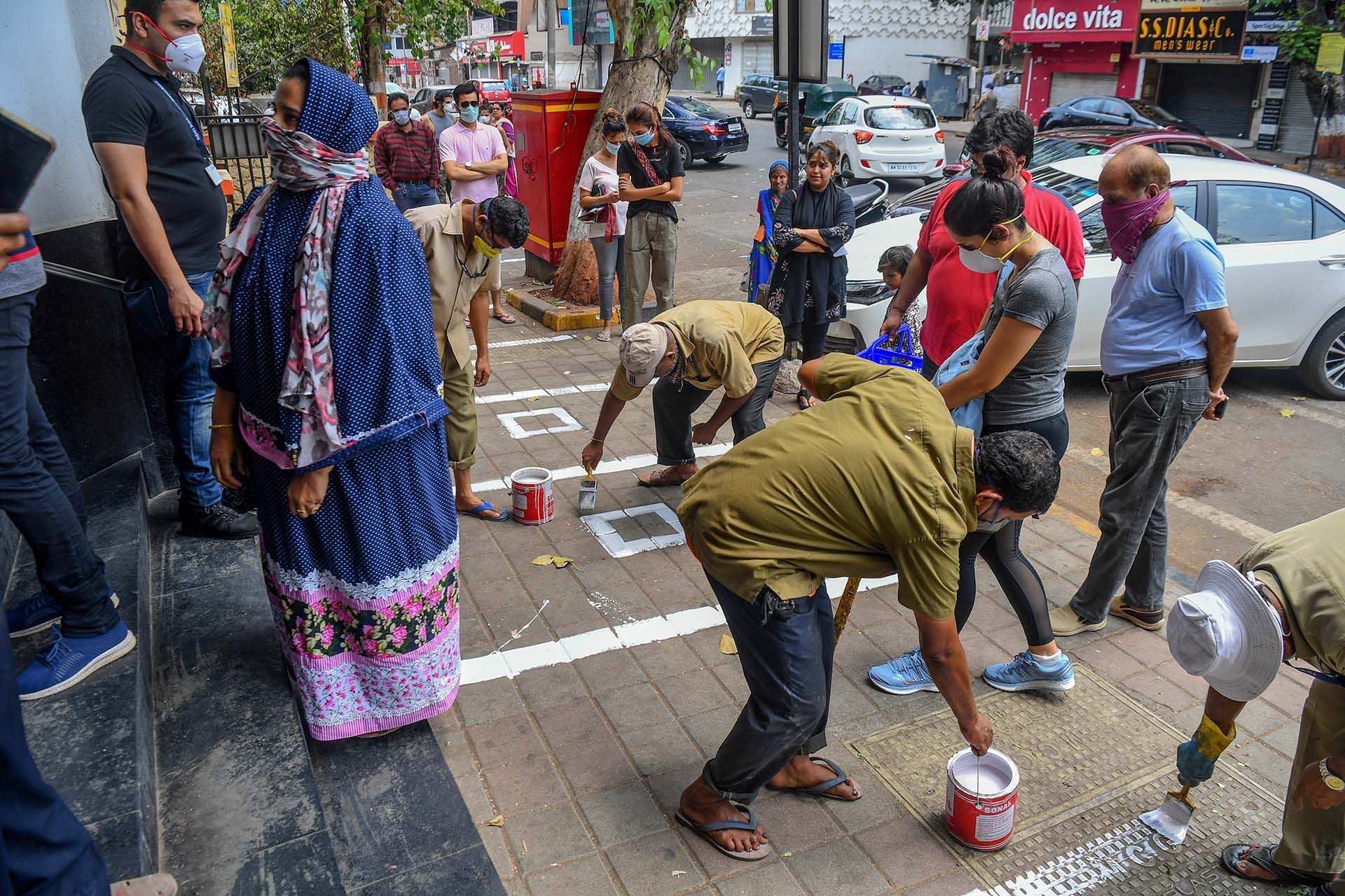 Trabajadores municipales pintan lineas en el suelo para mantener la distancia social frente a una tienda en Mumbai, India. 