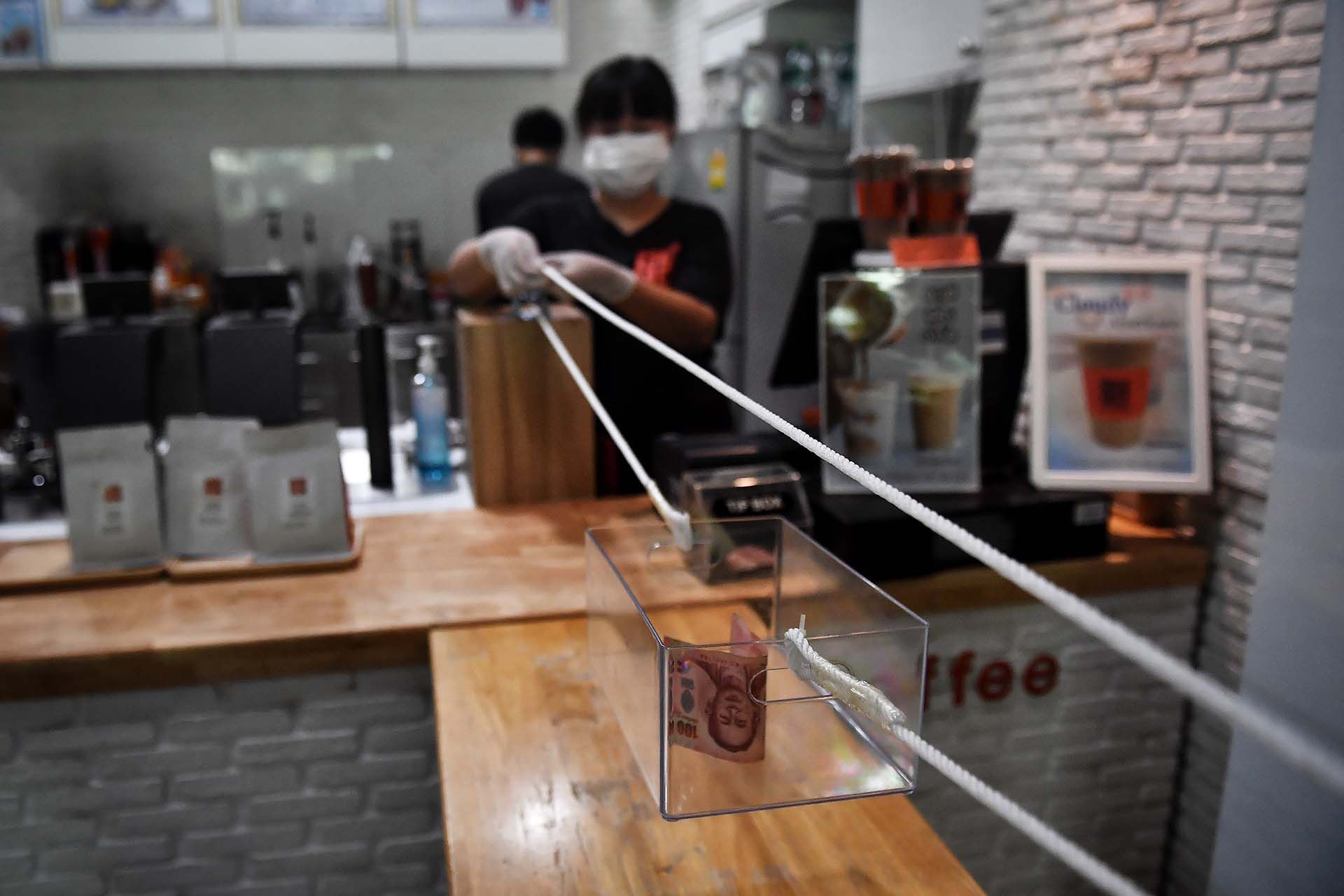 En la tienda "Art Of Coffee" de Bangkok idearon un método para recibir pago en dinero en efectivo de los clientes manteniendo la distancia social.