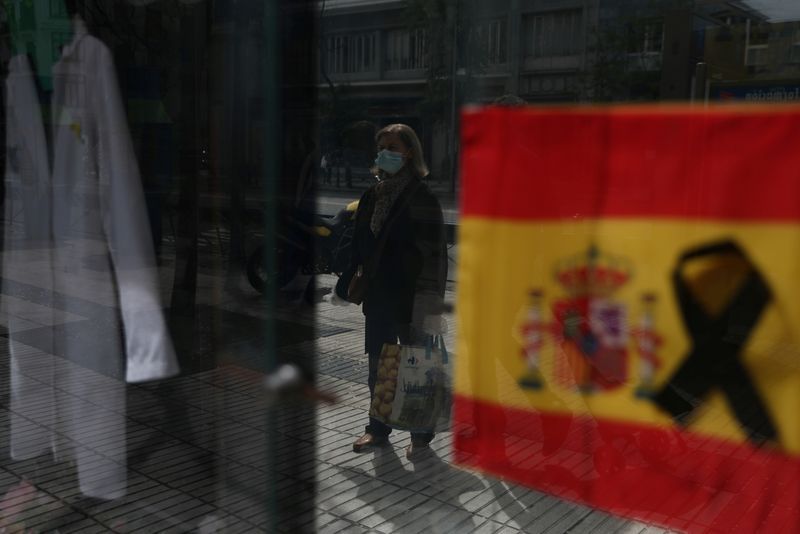 FILE PHOTO: A woman wearing a protective mask waits to enter a pharmacy displaying a Spanish flag with a black ribbon, amid the coronavirus disease (COVID-19) outbreak in Madrid, Spain, April 18, 2020. REUTERS/Susana Vera/File Photo