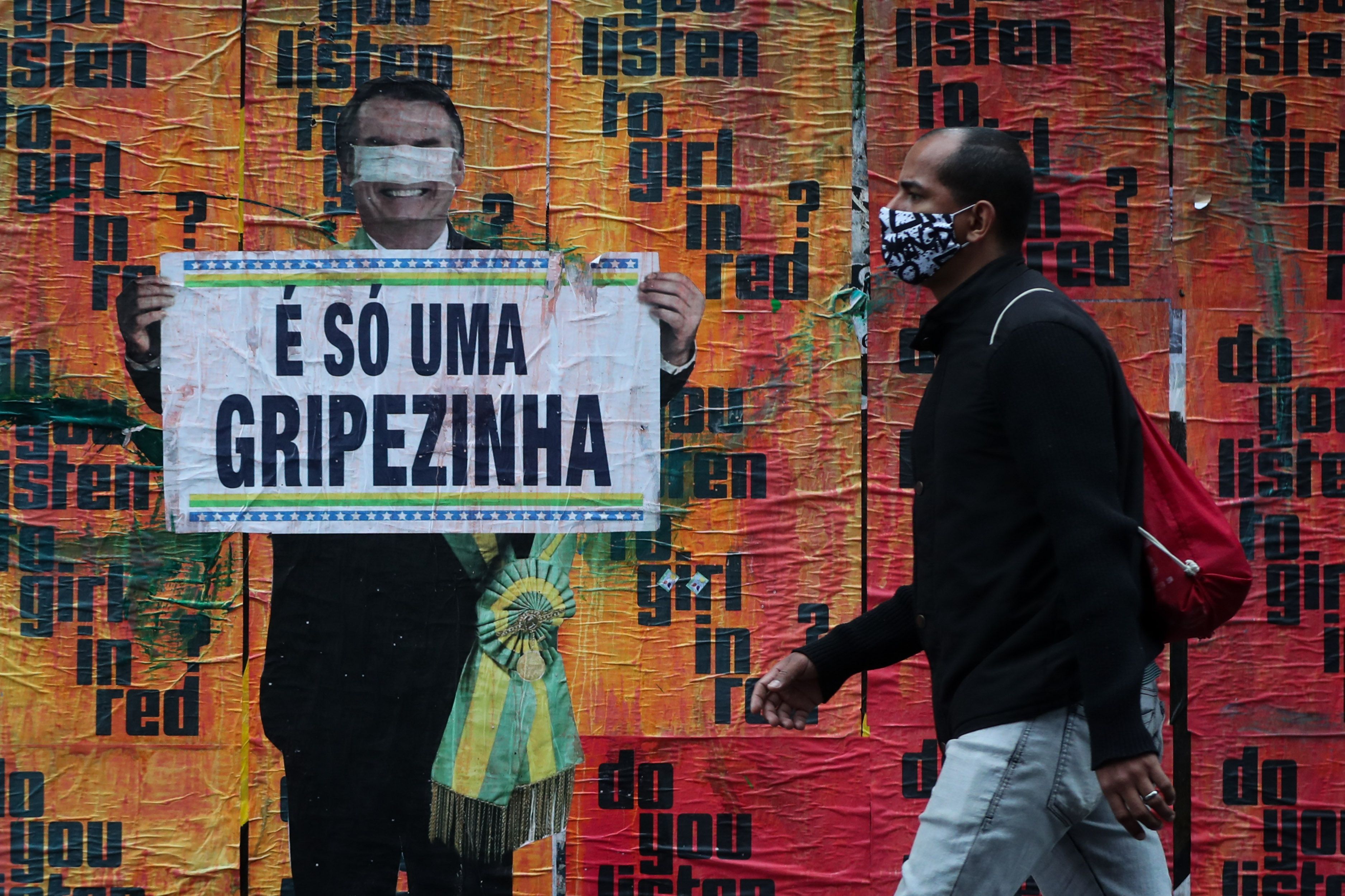 Un ciudadano camina hoy junto a una imagen del presidente brasileño Jair Bolsonaro sosteniendo un cartel con su polémico comentario sobre la COVID-19 al inicio de la pandemia. EFE/Fernando Bizerra 