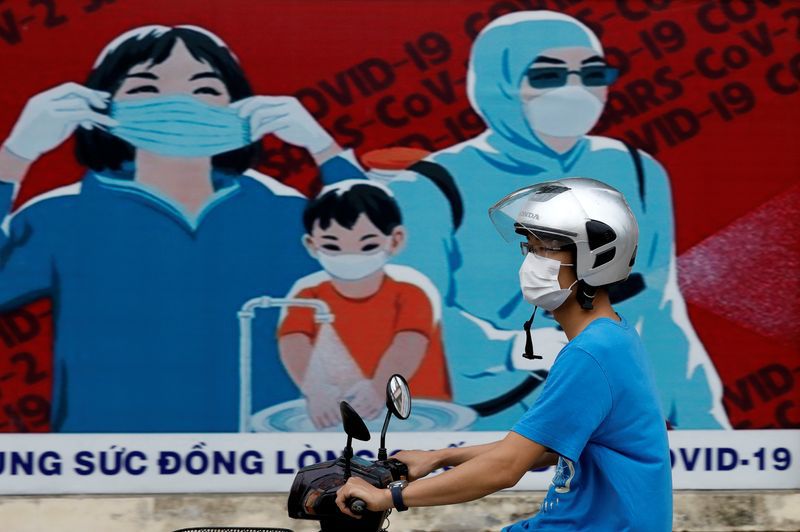 FOTO DE ARCHIVO: Un hombre con mascarilla pasa en motocicleta frente a un cartel para el fomento de la prevención contra la COVID-19 en Hanói, Vietnam, el 31 de julio de 2020. REUTERS/Kham
