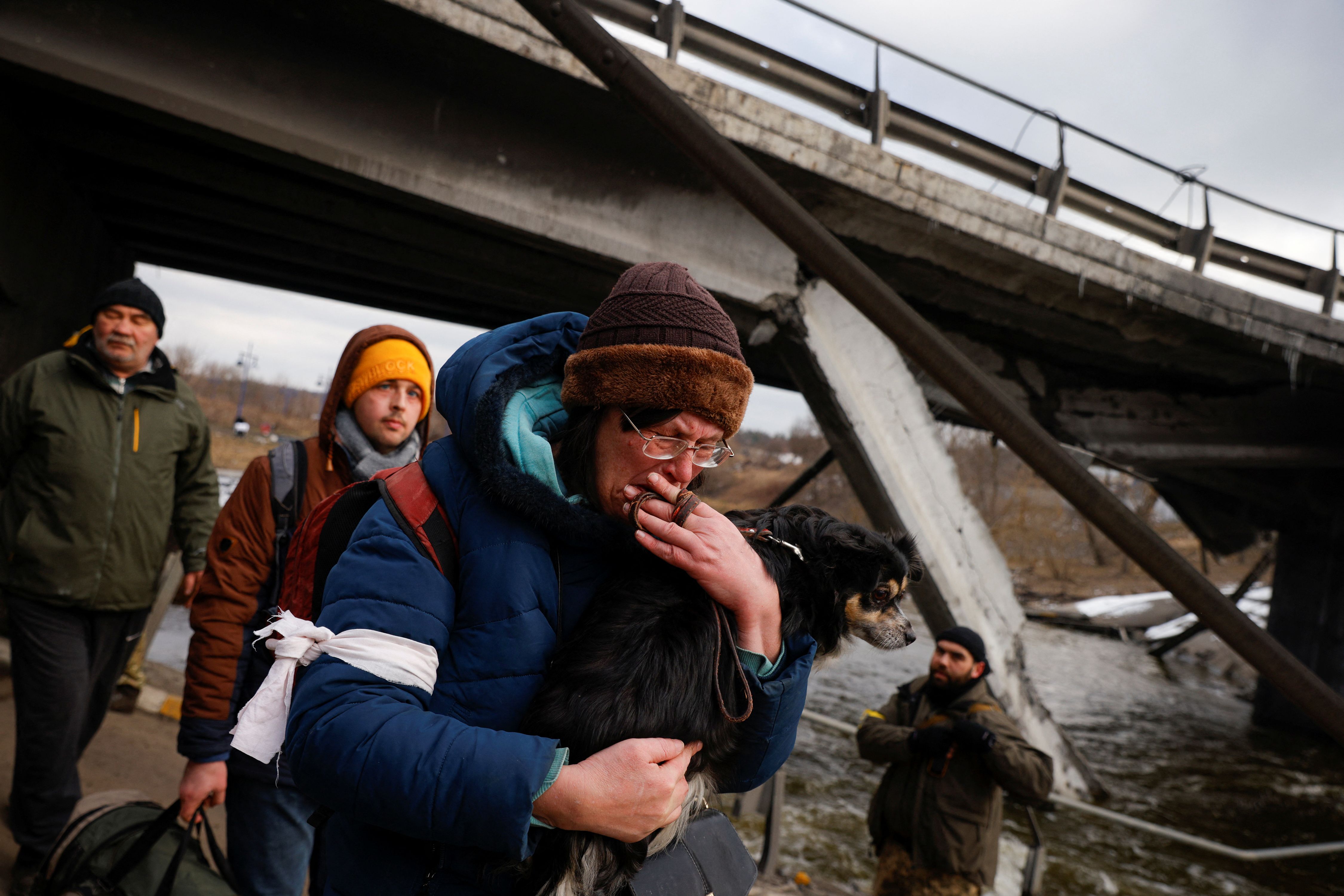 Un hombre sostiene a su perro mientras intenta pasar por un puente que fue destruido en un ataque ruso en Irpin (Reuters)