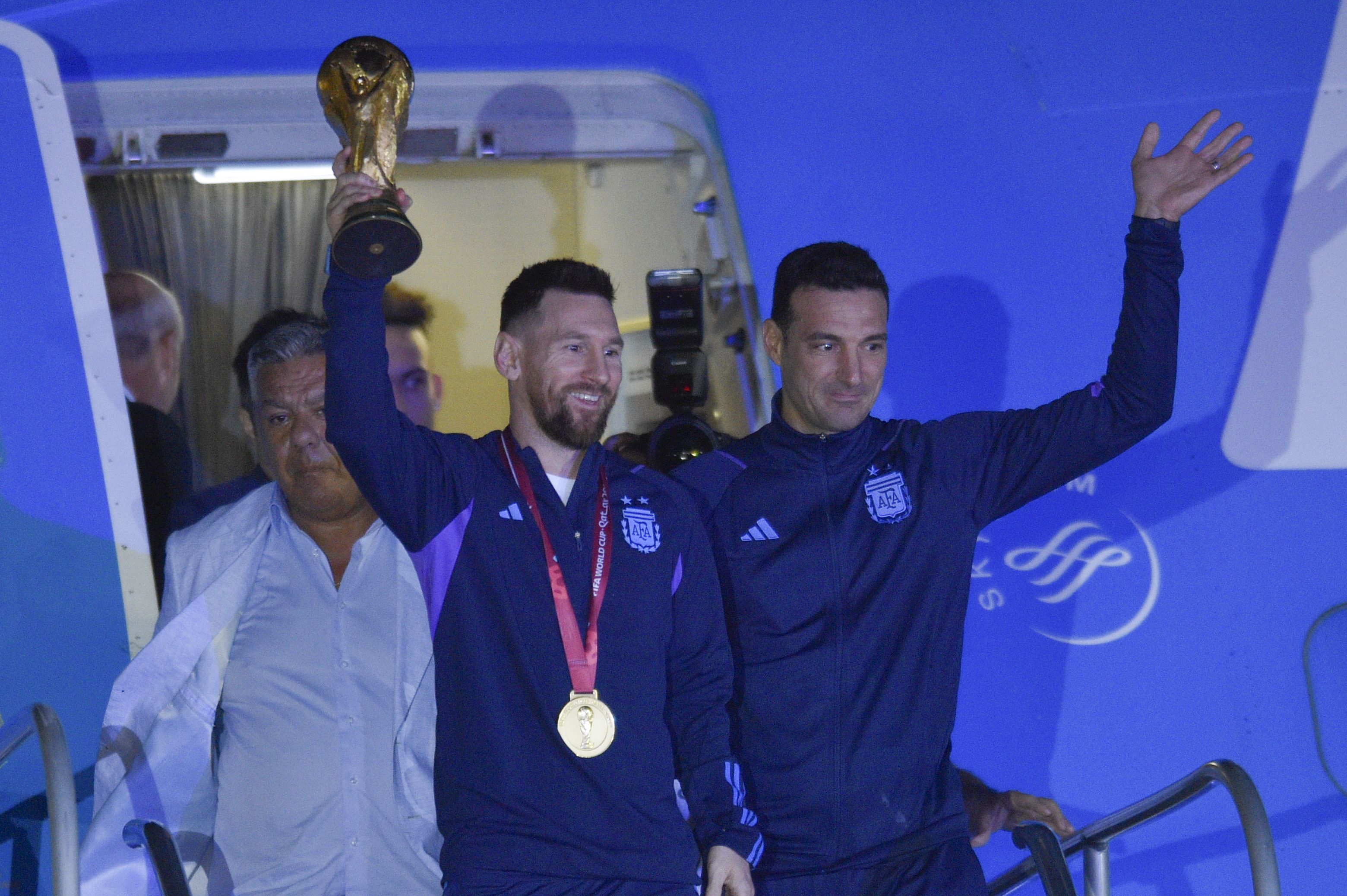 El futbolista argentino Lionel Messi sostiene el trofeo del Mundial de la FIFA a la salida de un avión junto al técnico Lionel Scaloni, en Buenos Aires, Argentina, el martes 20 de diciembre 2022. (AP Foto/Gustavo Garello)