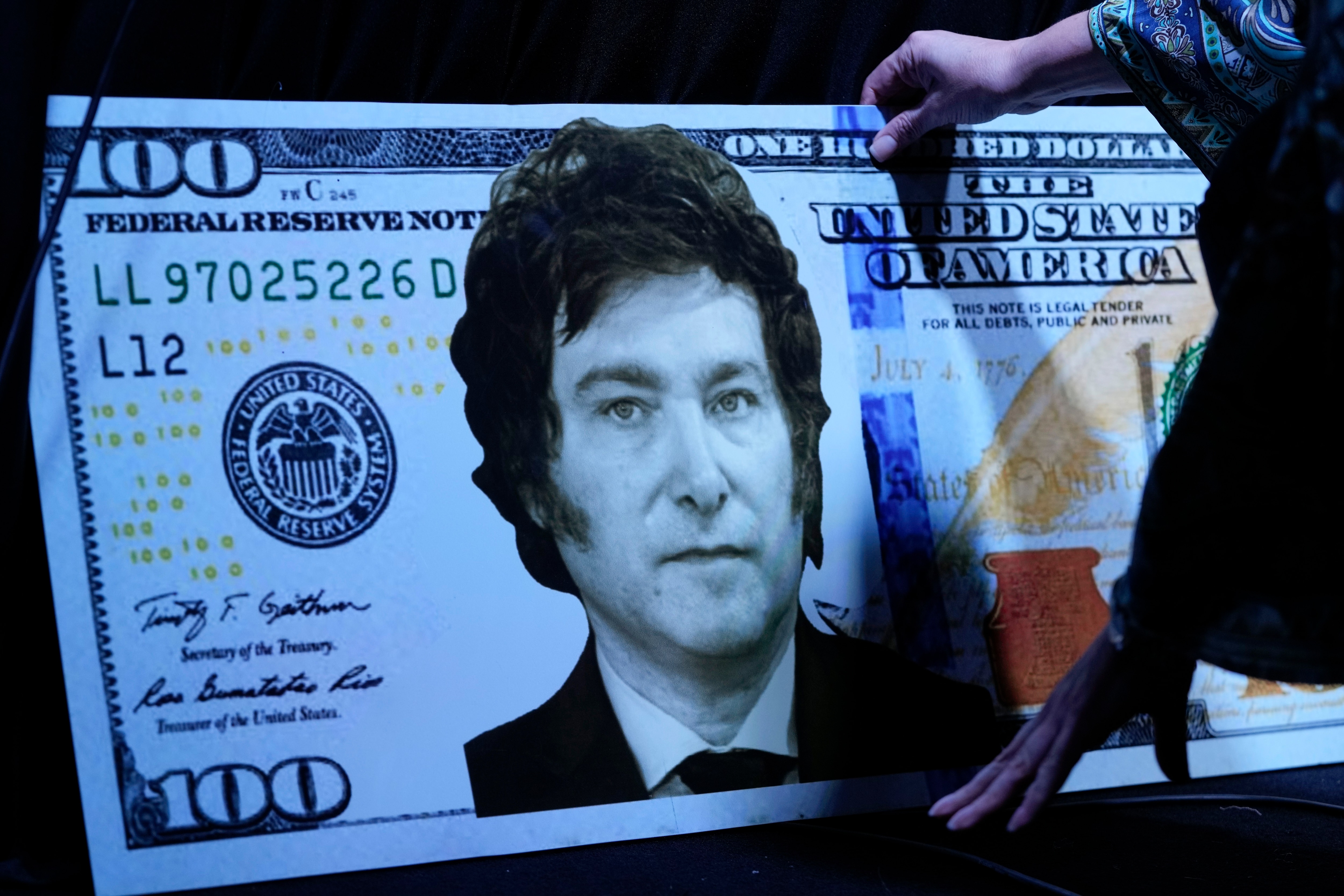 La hermana del candidato presidencial argentino Javier Milei, Karina Milei, coloca una foto de su hermano en un billete de cartón de 100 dólares antes del inicio de la presentación del libro de su hermano "El fin de la inflación" en la última Feria del Libro de Buenos Aires (AP)