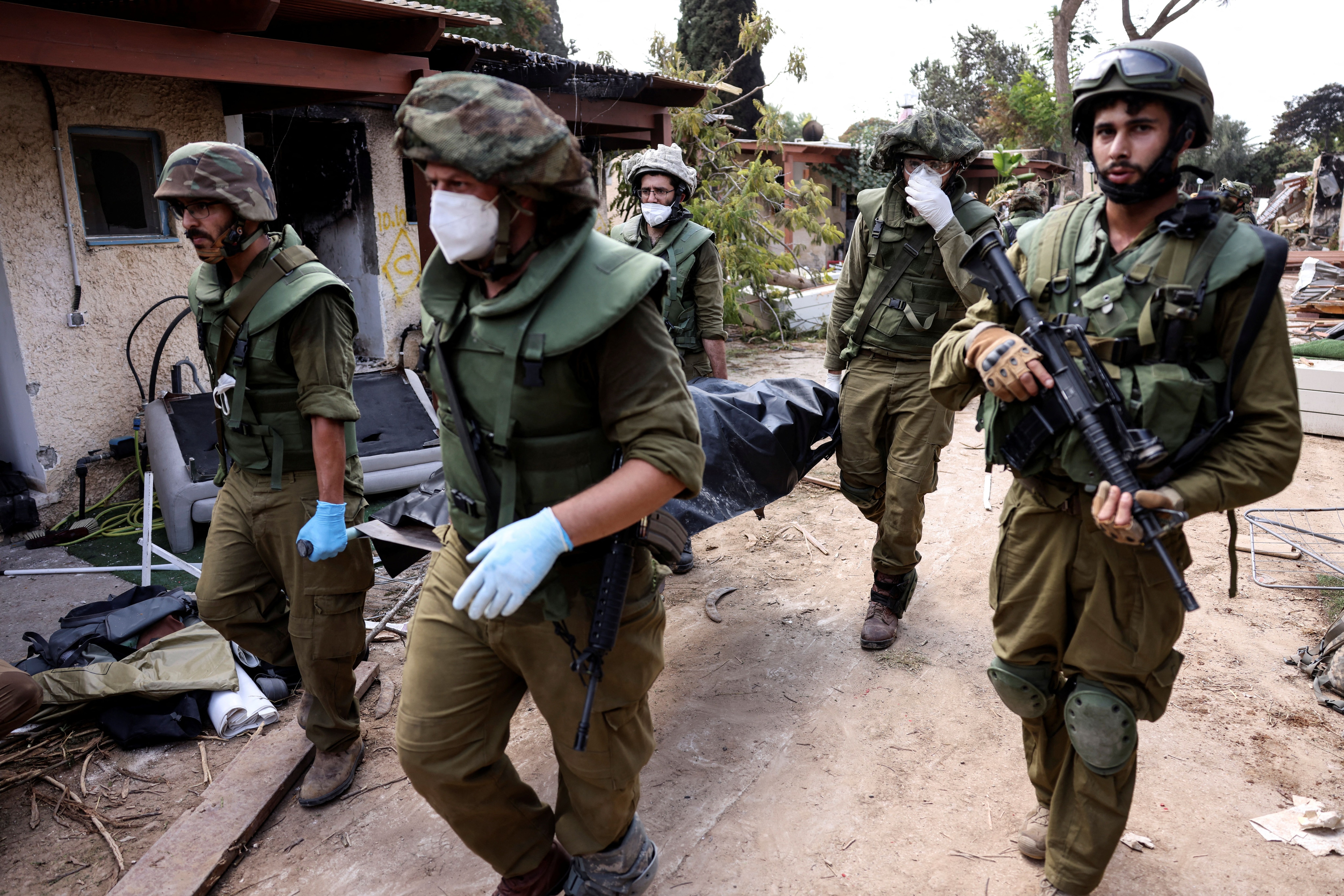 Soldados israelíes llevan un cadáver mientras recogen cuerpos tras los ataques desde Gaza en el kibutz Kfar Aza, en el sur de Israel, 10 de octubre de 2023 (REUTERS/Ronen Zvulun)