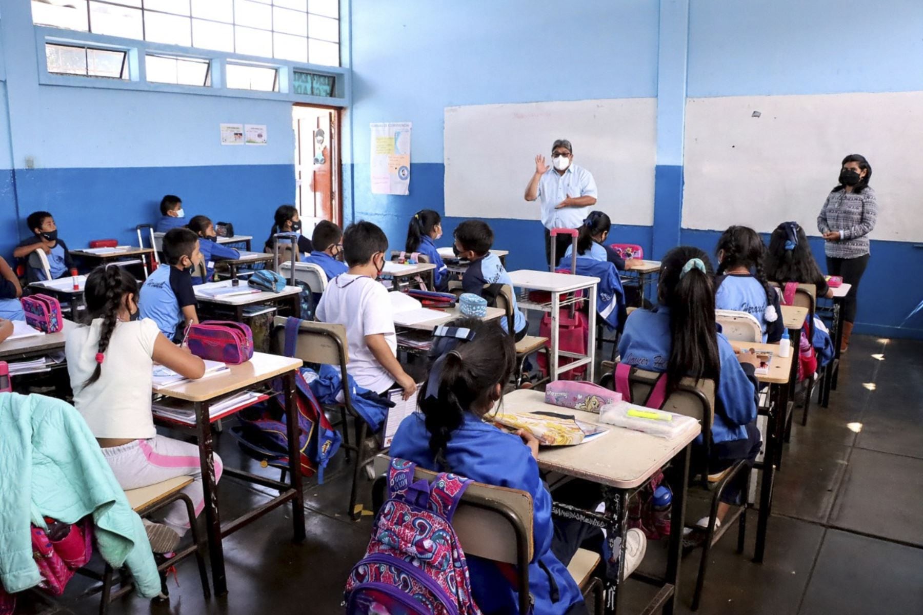 Imagen de un aula de clases, con estudiantes y maestros.